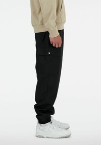 Pantalons cargo noirs avec poches latérales, poignets élastiques et coupe décontractée. Assortis à des baskets blanches. Le matériau semble durable.
