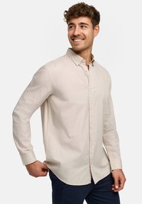 Beige langärmliges Hemd aus leichtem Stoff mit weicher Textur, ausgestattet mit einem Standardkragen, geradem Saum und sichtbaren Knöpfen.