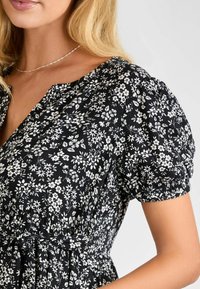 Abito nero floreale con maniche a sbuffo, caratterizzato da motivi di fiori bianchi, scollatura a V e vita arricciata, realizzato in tessuto leggero.