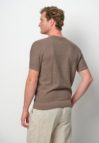 Brązowy sweter z krótkim rękawem o teksturowanym splocie, z okrągłym dekoltem i dopasowanym krojem, zestawiony z jasnymi lnianymi spodniami.