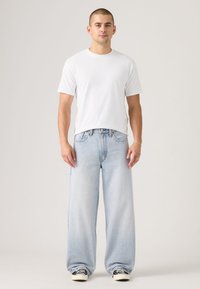 Light blue wide-leg jeans, cotton fabric, high-waisted design, frayed hem, paired with a plain white short-sleeve t-shirt and black sneakers.