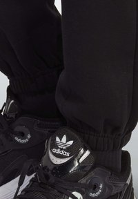 Black athletic shoes with glossy accents, textured mesh, and a prominent Adidas logo. The pants have an elastic cuff design.