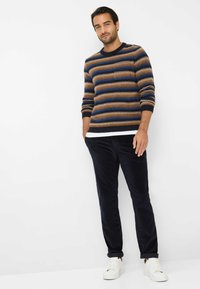 Gebreide trui met horizontale strepen in blauw, bruin en crèmekleur. Gepaard met donkere corduroy broek en witte sneakers.