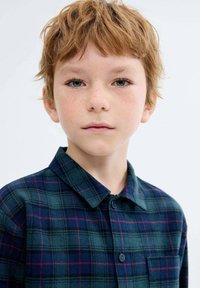 Karirana srajca z gumbom, ki ima temno zeleno podlago z rdečimi in mornarskimi črtami, izdelana iz mehkega blaga s klasičnim ovratnikom in sprednjo žepom.