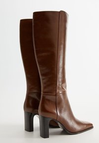 Bottes hautes jusqu'au genou en cuir marron avec une finition brillante, bout carré et talon noir épais. Présentent des coutures verticales le long de la tige.