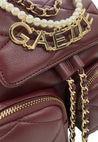 Borsa in pelle bordeaux con texture trapuntata, una tracolla in catena dorata e un accento di perle con il nome "GAËLLE" in lettere dorate.