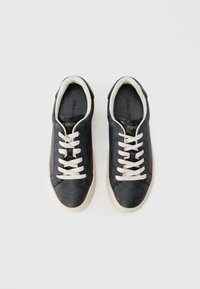 Μαρινό μπλε δερμάτινα αθλητικά παπούτσια με ομαλή υφή, μπεζ κορδόνια και αντιθετική σόλα από καουτσούκ. Διαθέτουν το λογότυπο Coach στην εσωτερική σόλα.