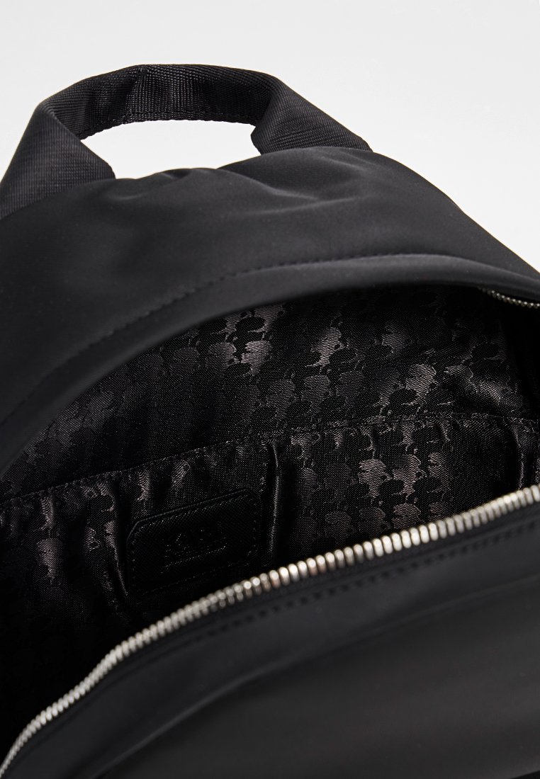 Sac à dos noir avec un extérieur lisse et une ouverture zippée révélant un intérieur noir texturé avec un motif subtil et une étiquette.