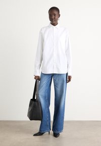 White button-up shirt with long sleeves, paired with wide-leg blue jeans. Holding a black leather tote bag. Pointed black heels.