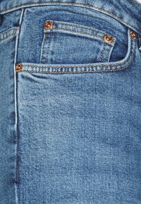 Blå denimjeans med en klassisk femficksdesign, med koppardetaljer, synlig sömnad och en lätt urtvättad textur.