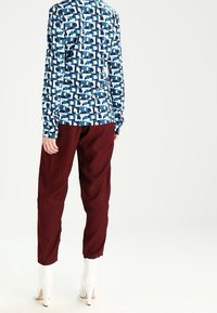Long-sleeve shirt in blue with geometric pattern, paired with burgundy pants. Both made from soft materials; white heeled boots add contrast.