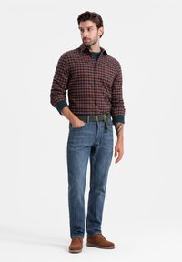 Camicia a maniche lunghe a quadri in ruggine e blu, abbinata a jeans blu. Cintura marrone e scarpe slip-on in suede marrone. Maglietta verde sotto visibile.