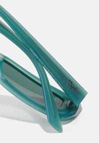 Ochelari de soare Aqua cu rame din material bio, design elegant și lentile întunecate, având logo-ul argintiu Ray-Ban pe brate.