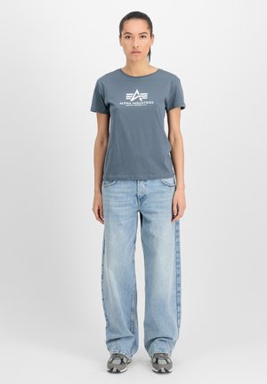 Grå bomulds t-shirt med et hvidt logo, parret med lyseblå brede jeans og grå sneakers med et stribet design.