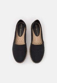 Zapatos negros sin cordones con parte superior texturizada, plantilla de yute marrón y costuras de color crema a lo largo de los bordes. Logo estampado en la parte frontal.