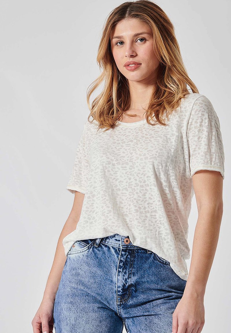 T-shirt à manches courtes de couleur beige clair avec un motif léopard, présentant une coupe décontractée et un col rond, associé à un jean bleu taille haute.