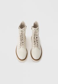 Botas de combate de cuero blanco con cordones frontales, puntera redonda y suela de goma marrón. Presentan altura hasta el tobillo y cremallera lateral para un fácil uso.