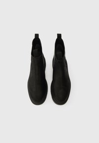 Bottes de cheville en cuir noir avec une texture lisse, bout arrondi et languettes à l'arrière pour un enfilage facile. Semelle en caoutchouc plate.