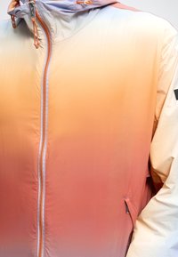 Ελαφρύ μπουφάν με κουκούλα και διαβαθμισμένα χρώματα από μπεζ σε πορτοκαλί, με μπροστινό φερμουάρ και μικρή τσέπη στη δεξιά πλευρά.