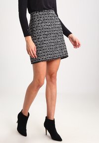 Svart-vit rutmönstrad kjol med en figursydd form, textilstruktur och sömlös fåll, kombinerad med svarta ankelskor.