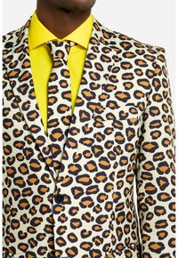 Leopardenmuster-Anzugjacke in Creme, mit schwarzen und orangefarbenen Punkten. Darunter ein gelbes Hemd und eine Krawatte für den Kontrast. Mit einer Brusttasche.