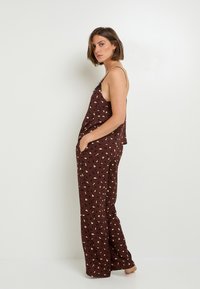 Ensemble de pyjama bordeaux avec imprimé léopard en crème et noir. Dispose de bretelles spaghetti et de poches dans le pantalon à jambe large. Texture de tissu lisse.