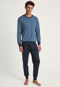 Marineblauwe langetermijn top met een zak en contrasterende kraag, gecombineerd met donkere joggingbroeken met elastische boorden. Zacht, gemêleerd stof.