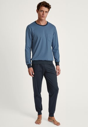 Marineblauwe langetermijn top met een zak en contrasterende kraag, gecombineerd met donkere joggingbroeken met elastische boorden. Zacht, gemêleerd stof.