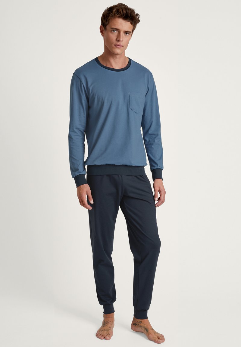 Marineblauwe langetermijn top met een zak en contrasterende kraag, gecombineerd met donkere joggingbroeken met elastische boorden. Zacht, gemêleerd stof.