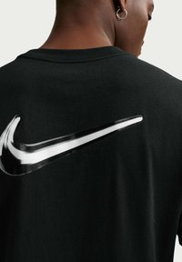 Κοντινό πλάνο ενός ατόμου που φοράει μαύρο πουκάμισο με μεγάλο λευκό και μαύρο λογότυπο Nike swoosh στον πίσω ώμο.