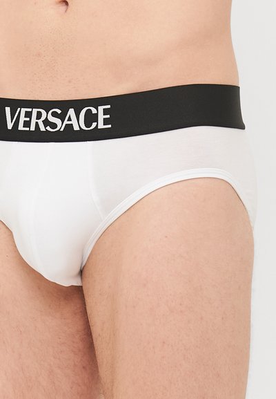 Fehér pamutzokni fekete derékrésszel, amelynek fehér felirata VERSACE. Simaság jellemzi, és testhezálló fazonnal rendelkezik.