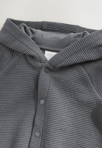 Dark gray textured baby hoodie with snap buttons and a sewn-in label inside the collar area.