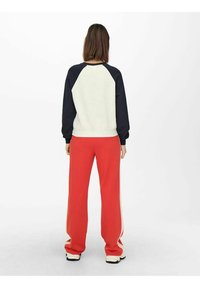 Sudadera con mangas raglán en crema y azul marino, combinada con pantalones de pierna ancha rojos con paneles laterales en crema, tela suave y corte relajado.