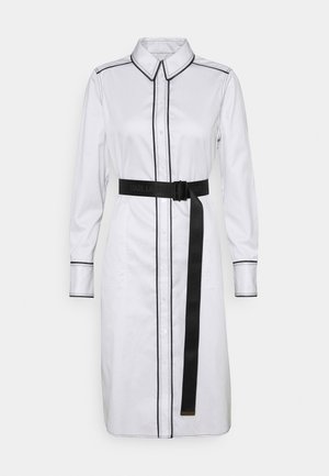 White long-sleeve shirt dress with black contrast stitching, front buttons, collar, and a black belt with a long hanging strap.