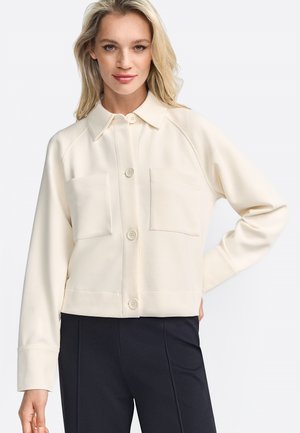 Crème-kleurige button-up shirt met kraag, twee borstzakken en lange mouwen. Glad materiaal met een iets cropped pasvorm.