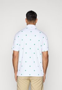 Πόλο μπλουζάκι κοντό μανίκι από λευκό ύφασμα, με πράσινο γεωμετρικό σχέδιο. Κλασικό γιακά με κουμπιά και χαλαρή εφαρμογή.