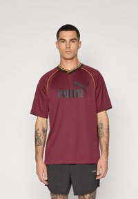 Bordeaux sportshirt met V-hals, gele snit en zwart "PUMA"-logo. Gemaakt van een structuurstof, met korte mouwen en een ontspannen pasvorm.