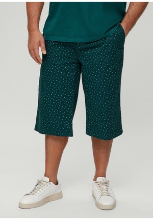 Grüne Shorts mit einem gepunkteten Muster, aus weichem Material. Verfügt über Taschen und einen geraden Schnitt, kombiniert mit weißen Sneakers.
