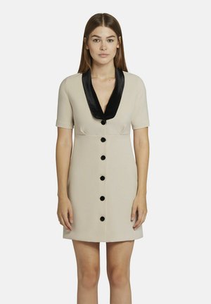 Robe beige à manches courtes, col en satin noir et boutons noirs sur le devant. Texture lisse, coupe ajustée, longueur au-dessus du genou.
