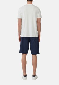 Witte t-shirt met korte mouwen en een ronde hals, gecombineerd met marineblauwe shorts. Het model draagt witte sneakers met marineblauwe accenten.