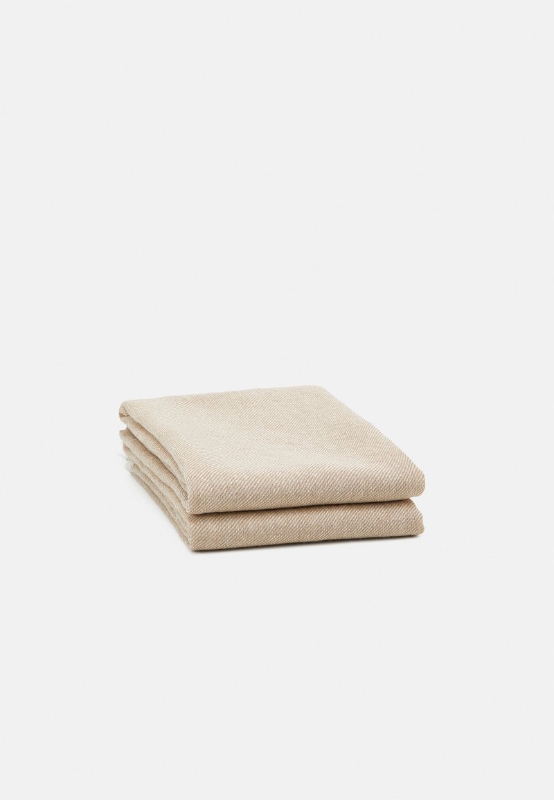 Couverture en laine beige pliée avec un motif chevrons subtil, posée sur un fond blanc.