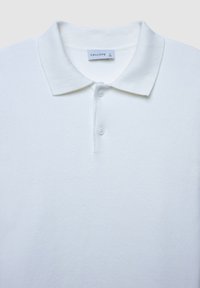 Weißes Poloshirt aus strukturiertem Stoff, mit klassischem Kragen, Drei-Knopf-Leiste und einem Markenetikett im Nacken.
