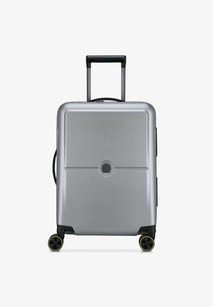 Valigia rigida argentata con finitura lucida, manico telescopico, due ruote nere con accenti gialli e un logo circolare centrato.