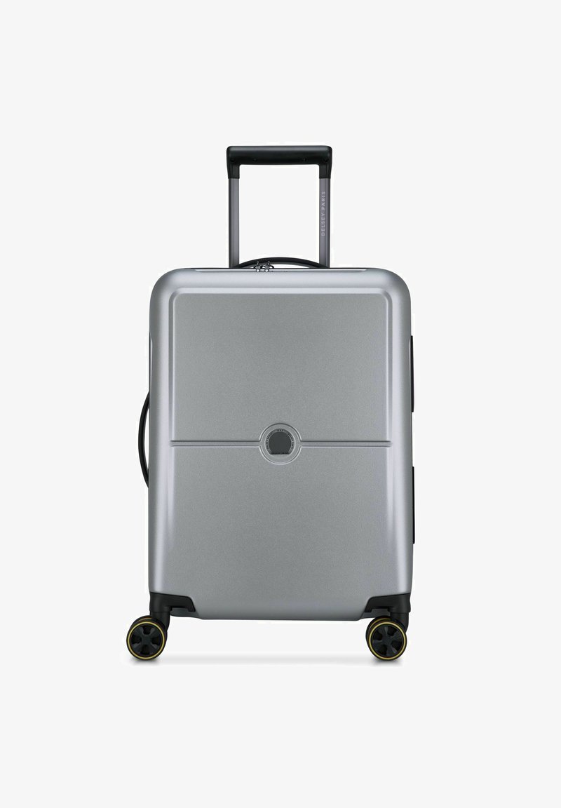 Valigia rigida argentata con finitura lucida, manico telescopico, due ruote nere con accenti gialli e un logo circolare centrato.