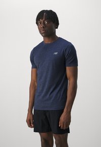T-shirt de sport bleu marine en tissu texturé, avec des manches courtes et un logo subtil sur la poitrine, accompagné de shorts noirs.
