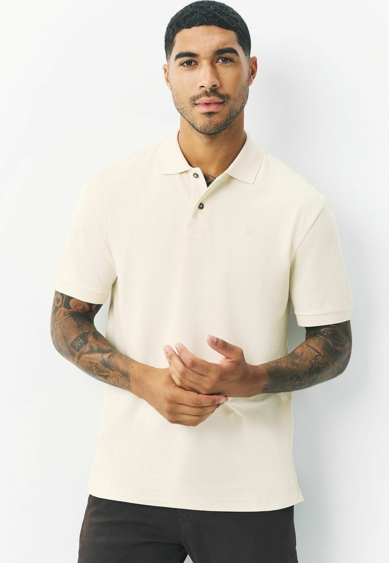 Beige polo-shirt met een klassieke kraag, een knoopsluiting met twee knopen en een subtiele logo op de borst; gladde textuur en korte mouwen.