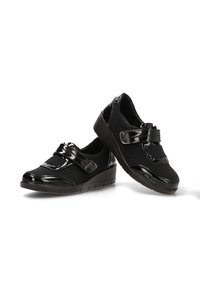 Scarpe nere con finitura lucida in pelle verniciata, un cinturino in velcro e una tomaia testurizzata con dettagli perforati. Suola leggermente a cuneo.