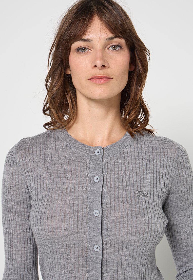 Grauer gerippter Cardigan aus Strickmaterial, mit rundem Ausschnitt, Knopfverschluss und kleinem Logo auf der linken Seite.