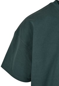 Tricou din bumbac verde închis, cu un croi lejer, mâneci scurte și o textură netedă, având un gât rotund.