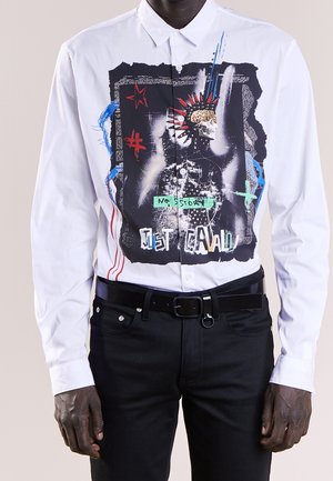 Witte overhemd met knopen featuring een grote grafische ontwerp met een schedel en kleurrijke accenten, gecombineerd met zwarte jeans en een riem.